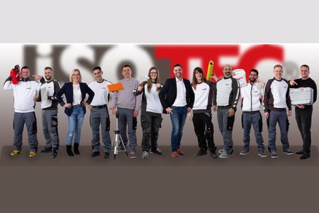 ISOTEC Team posiert frontal mit Werkzeugen vor großem Logo.